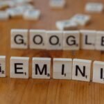 Scrabble tiles spelling out Google and Gemini on a wooden table, focusing on AI concepts.